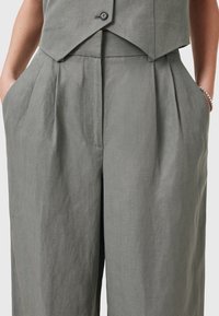 Svetle šedé lněné kalhoty s volným střihem, se skladbami, bočními kapsami a hladkým povrchem. Vhodné do teplého počasí.