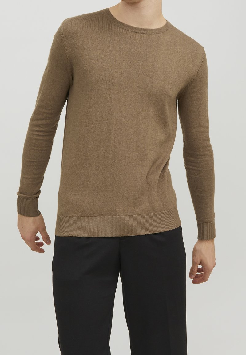 Pull léger marron en maille avec manches longues, poignets et ourlet côtelés, col rond et texture fine. Assorti à un pantalon sombre.
