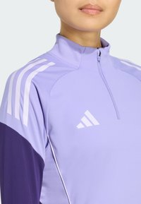 Purple athletic zip-up top with a high collar, featuring white three-stripe accents on shoulders and an embroidered logo on the chest.