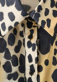 Camicia con stampa leopardata caratterizzata da una combinazione di colori crema e nero, con colletto classico, bottoni e una texture di tessuto liscia.