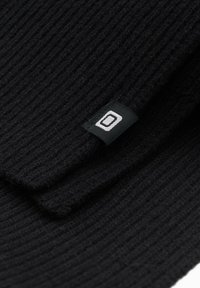 Tissu noir côtelé avec un design plié, présentant une petite étiquette tissée arborant un logo géométrique blanc sur fond noir.