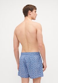 Blå mønstrede shorts laget av lett stoff med elastisk liv. Har et blomsterdesign og faller over kneet.