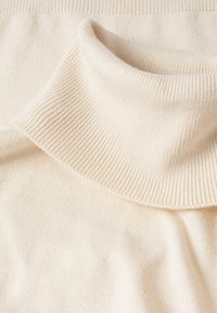 Tissu de pull à col roulé côtelé couleur crème montrant une texture douce en tricot et un détail de col plié.