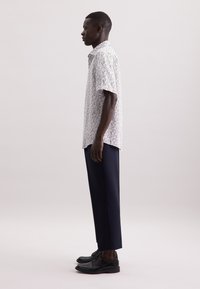 Korte mouwen, wit shirt met kleurrijk bloemenpatroon, gecombineerd met marineblauwe broek en zwarte schoenen. Glad stof en getailleerde pasvorm.