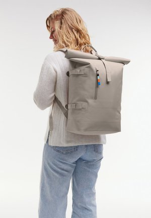 Mochila gris tipo roll-top hecha de un tejido duradero, con correas ajustables, un bolsillo con cremallera frontal y acentos coloridos en los tiradores de la cremallera.