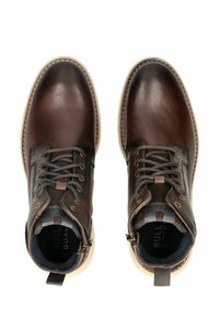 Botas de cuero marrón hasta el tobillo con punteras redondas, suelas beige en contraste, cordones delanteros, cremallera lateral y forro de tela azul.