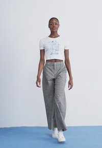 Hvid cropped t-shirt med blå grafisk tekst, parret med højtaljede grå ternede vide bukser og hvide sneakers.
