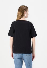 Zwarte katoenen t-shirt met korte mouwen, een relaxte pasvorm en een ronde halslijn. Draagt een lichtblauwe spijkerbroek.