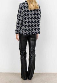 Jas met een houndstoothpatroon in grijs en marineblauw met een ontspannen pasvorm, gecombineerd met strakke zwarte neplederen broek en enkellaarsjes.