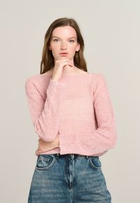 Hellrosa, gestrickter Pullover mit langen Ärmeln und U-Boot-Ausschnitt, kombiniert mit hoch geschnittenen, ausgewaschenen blauen Jeans. Weicher, strukturierter Stoff.