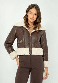 Giubbotto corto in pelle marrone con collo e polsini in shearling bianco, dotato di tasche con zip argentata e chiusura frontale con zip.