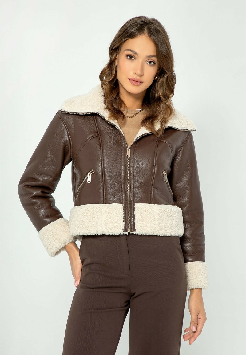 Giubbotto corto in pelle marrone con collo e polsini in shearling bianco, dotato di tasche con zip argentata e chiusura frontale con zip.
