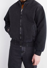Czarna bomberka z denimu, z długimi rękawami, ściągaczami na mankietach i dole, przednim suwakiem oraz bocznymi kieszeniami; wykonana z gładkiej, fakturowanej tkaniny.