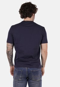T-shirt blu navy a maniche corte in cotone, con scollo rotondo e una texture liscia. Indossato con jeans di denim blu sbiaditi.
