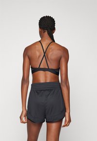 Svart sportsbh med kryssrygg, parret med svarte løpeshorts med rynket midjebånd og sidetreninger for enkel bevegelse.