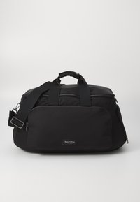 Sac de sport en nylon noir avec double poignées, sangle réglable, poche zippée à l'avant et étiquette de marque. Texture lisse et forme structurée.
