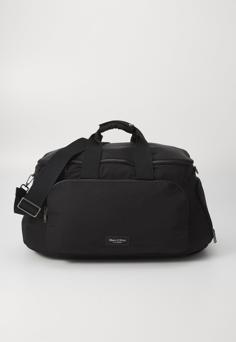 Sac de sport en nylon noir avec double poignées, sangle réglable, poche zippée à l'avant et étiquette de marque. Texture lisse et forme structurée.