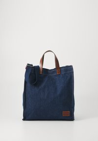 Denim tas met bruin leren handvatten, rechthoekige vorm en een afneembare schouderriem. Beschikt over een leren label aan de voorkant.