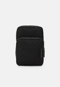 Zaino nero con trama trapuntata, tasca frontale con zip e dettagli discreti del logo. Presenta tessuto liscio e forma strutturata.