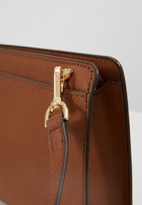 Borsa a tracolla in pelle marrone con texture, con hardware dorato, caratterizzata da una zip e dettagli di cucitura. Design compatto con una finitura pulita.