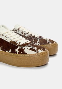 Sneakers din piele de vacă maro și alb cu șireturi crema, talpă groasă din cauciuc și textură fină. Prezintă detalii de cusătură și un design cu profil jos.