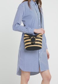 Liten crossbody-väska med randig halmdesign i beige och svart, med ett svart läderlock och ett guldspänne som accent.