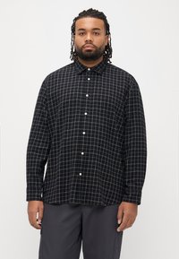 Camisa xadrez preta com gola abotoada, botões brancos e corte descontraído. Apresenta um padrão quadriculado em cor clara contrastante.