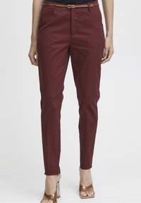 Pantalons taillés bordeaux avec une coupe ajustée, dotés de passants de ceinture et d'une ceinture en cuir marron. Tissu lisse avec des plis sur le devant et des poches latérales.