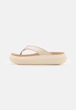 Tongs beige à semelle épaisse, avec une bride en tissu doux et une semelle matelassée, présentées de côté sur fond blanc.