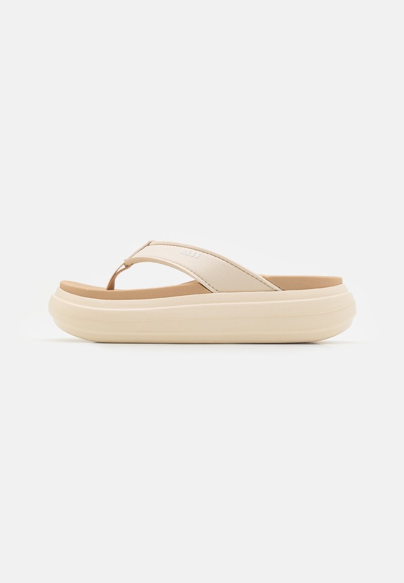 Tongs beige à semelle épaisse, avec une bride en tissu doux et une semelle matelassée, présentées de côté sur fond blanc.