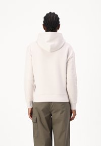 Sudadera de color beige claro con capucha ajustable, puños y dobladillo acanalados. Combinada con pantalones cargo, que presentan una textura suave y un corte relajado.