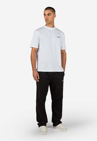 Weißes Baumwoll-T-Shirt mit Rundhalsausschnitt und kurzen Ärmeln, kombiniert mit schwarzen Hosen mit Logodetail und weißen Sneakers.