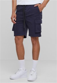 Marinefarbene Cargo-Shorts mit Zugbandbund, seitlichen Taschen und einem lockeren Schnitt. Hergestellt aus leichtem Material. Tragen Sie dazu weiße Sneaker und Socken.