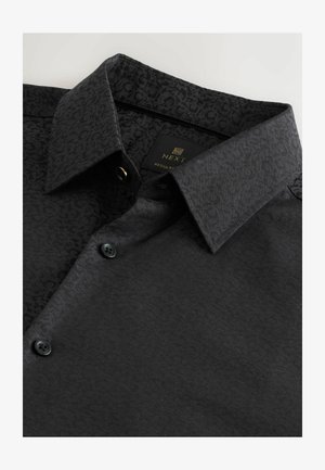 Chemise noire avec un motif texturé, dotée d'un col structuré, de deux boutons et d'une étiquette. Le matériau est lisse avec une finition douce.