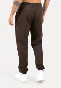 Pantalones de chándal marrones fabricados con material suave, con cintura elástica y piernas ajustadas, combinados con zapatillas blancas.