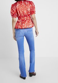Blusa de satén roja con puntos blancos, mangas abullonadas y cintura entallada, combinada con jeans de campana azul claro y botas de tacón marrones.