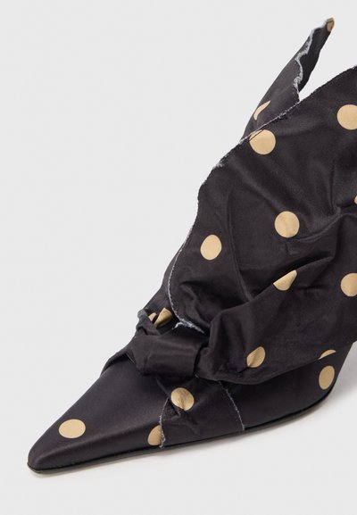 Musta kangas korkokenkä kultaisilla pilkuilla, jossa on terävä kärki ja drapeerattu, solmittu rakenne yläosassa. Elegantti muotoilu.