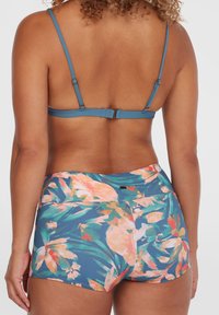 Blå bikiniöverdel med tunna remmar och knäppe; högmidjade shorts med blommönster i teal, rosa och gröna nyanser.