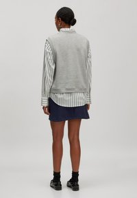 Grauer ärmelloser Sweatshirt über einem gestreiften Shirt in Weiß und Schwarz, kombiniert mit einem marineblauen Rock. Der Look zeichnet sich durch einen lässigen Schnitt und geschichtete Texturen aus.