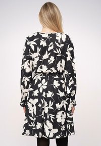 Vestido floral en blanco y negro con mangas largas, cintura ceñida con cinturón, corte fluido, puños fruncidos y una textura suave.