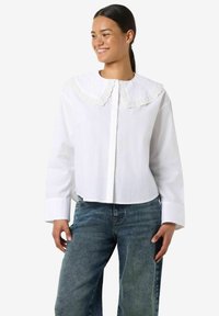 Biała krótka koszula z dużym, haftowanym koronkowym kołnierzem i długimi rękawami, wykonana z gładkiej bawełnianej tkaniny. Stylizowana z niebieskimi dżinsami z denimu.