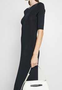 Robe midi noire côtelée ajustée à manches courtes, associée à un sac à main blanc avec une sangle noire texturée.