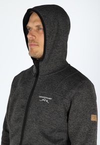 Donkergrijze fleece hoodie met ritssluiting, verstelbare capuchon en logo op de borst. Heeft textuurstof en leren accenten op de mouw.