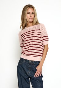 Knit short-sleeve džemperis gaiši rozā krāsā ar tumši sarkaniem svītrām. Strukturēta vaļīga auduma un ribota apakšmala, kopā ar brīviem tumšiem džinsiem.