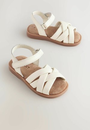 Sandalias de cuero blanco con tiras entrecruzadas, correa en el tobillo trasera y una suela texturizada marrón. Presenta una plantilla de suave gamuza.