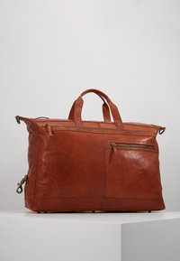 Sac de voyage en cuir de couleur brun riche, avec une texture lisse, deux poignées supérieures et une poche zippée extérieure pour plus de fonctionnalité.