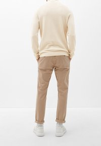 Pull beige en maille avec motif texturé, associé à un pantalon chino marron clair. Des baskets blanches et des ourlets retroussés complètent la tenue.