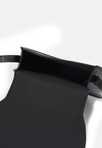 Borsa nera con un interno in tessuto liscio e un pattern di pelle di serpente testurizzata all'esterno. Aperta, che rivela un interno spazioso.