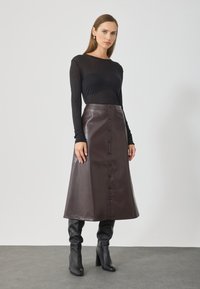 Falda midi de cuero marrón con botones en el frente, combinada con una blusa negra de manga larga y botas negras hasta el tobillo. Textura suave y diseño elegante.