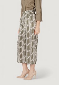 Pantaloni culotte con un motivo geometrico oliva e crema, caratterizzati da una vita alta, pieghe e un tessuto leggero. Indossati con tacchi alti beige.